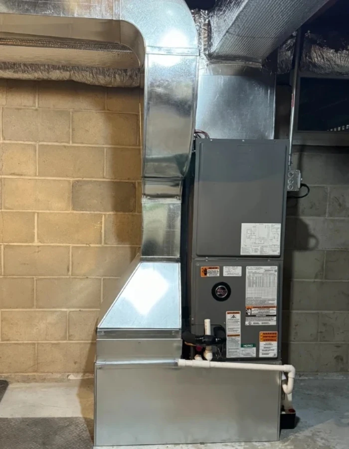 A gas furnace setup connected to metal ductwork. It has a condensate drain line and venting typical of a high-efficiency furnace.